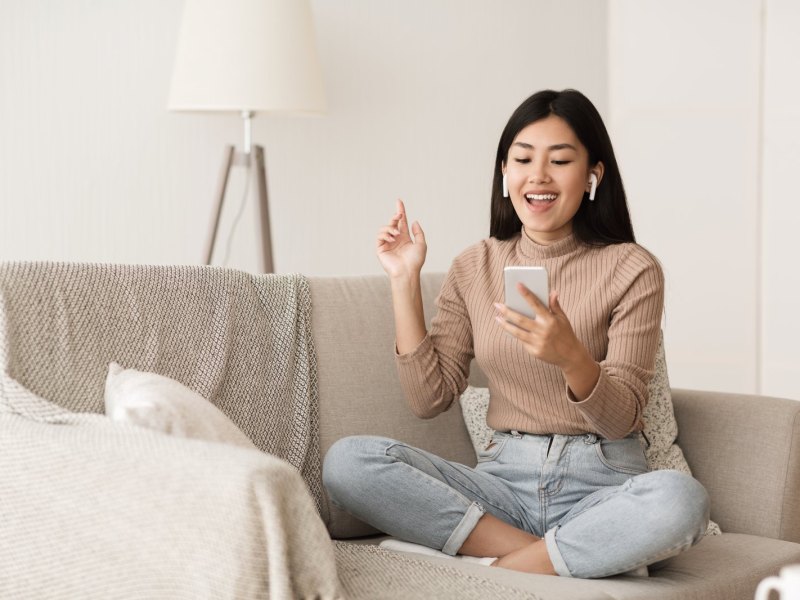 Frau sitzt auf dem Sofa und hat AirPods im Ohr.