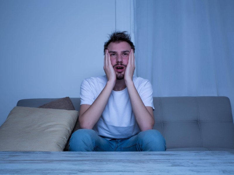 Mann sitzt auf dem Bett und guckt schockiert.