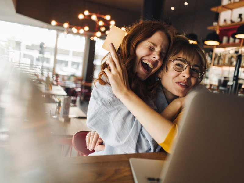 Zwei Frauen umarmen sich freudig vor einem Laptop.