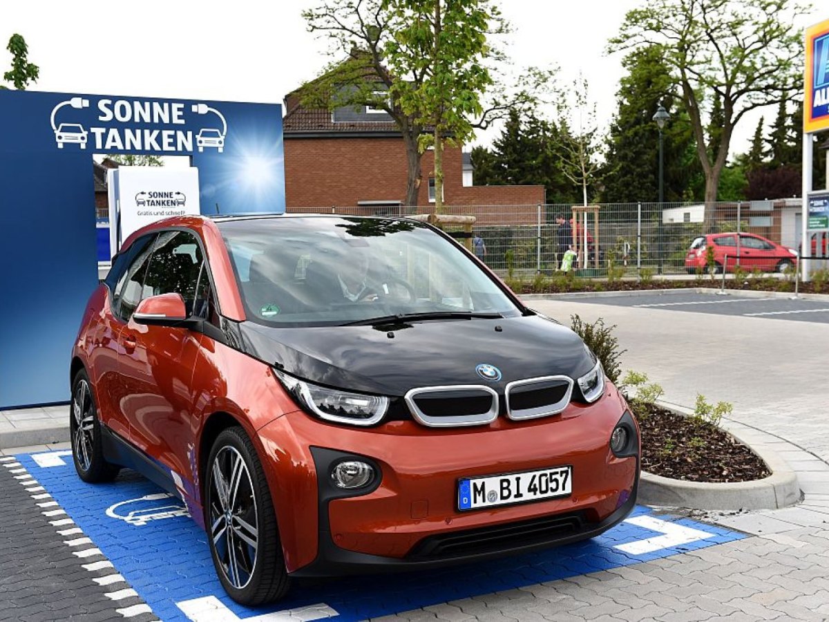 Ein Elektroauto von BMW steht vor einer Werbewand mit der Aufschrift "Sonne tanken".