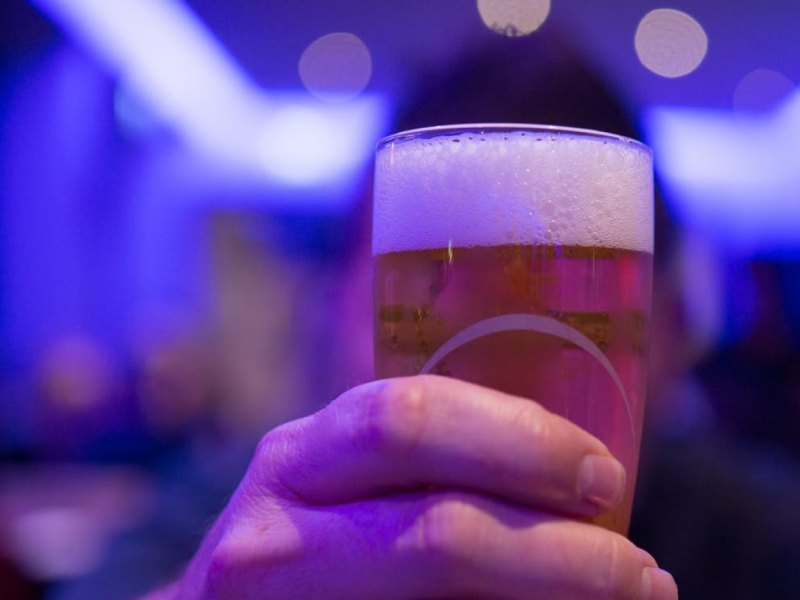 Eine Hand hält ein Glas Bier in einer dunkel ausgeleuchteten Location.