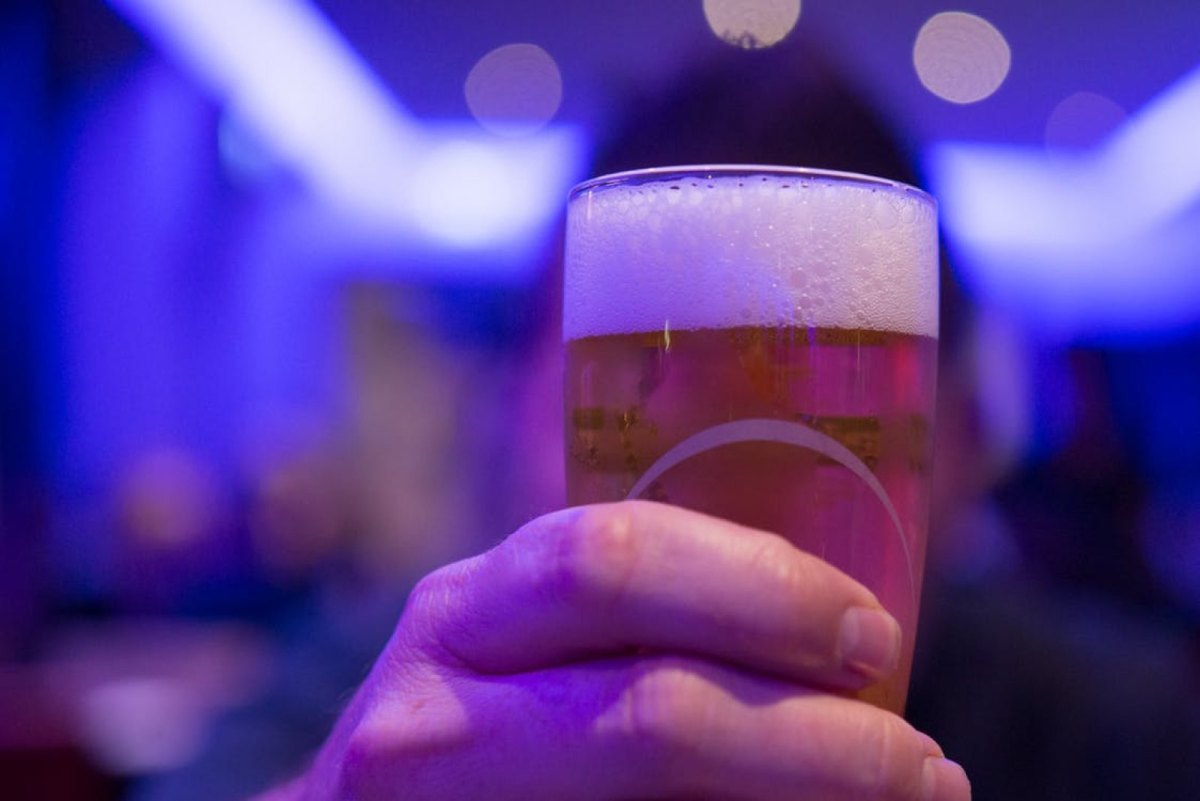 Eine Hand hält ein Glas Bier in einer dunkel ausgeleuchteten Location.