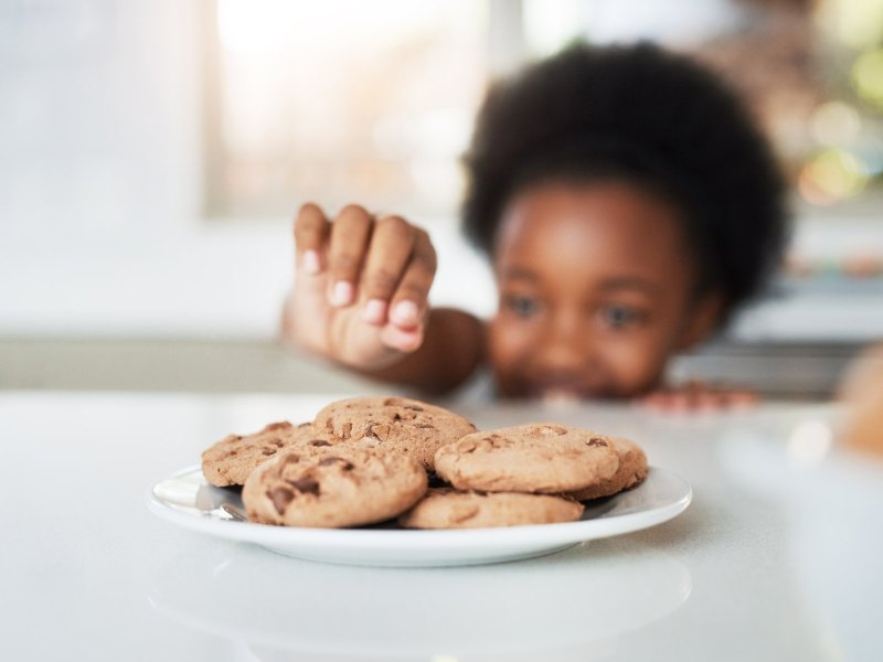 Kind stibitzt sich einen Cookie vom Teller.