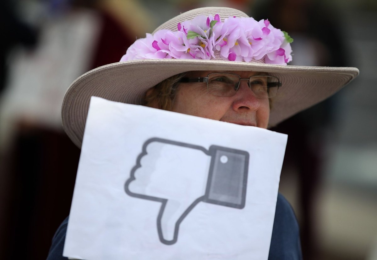 Eine Frau mit Hut hält ein Papierschild mit einem Facebook-Dislike-Button hoch.