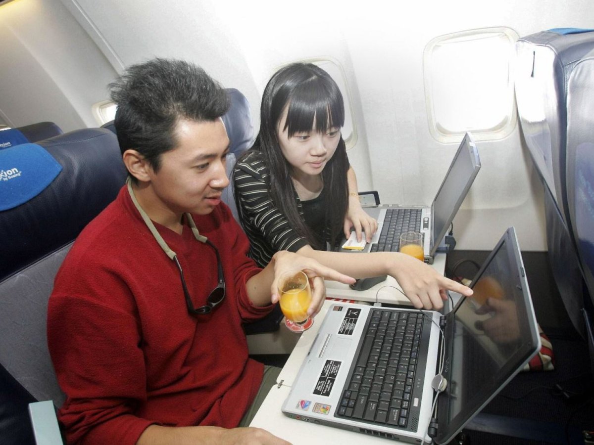 Zwei Menschen im Flugzeug schauen auf ihre Laptops und trinken Orangensaft