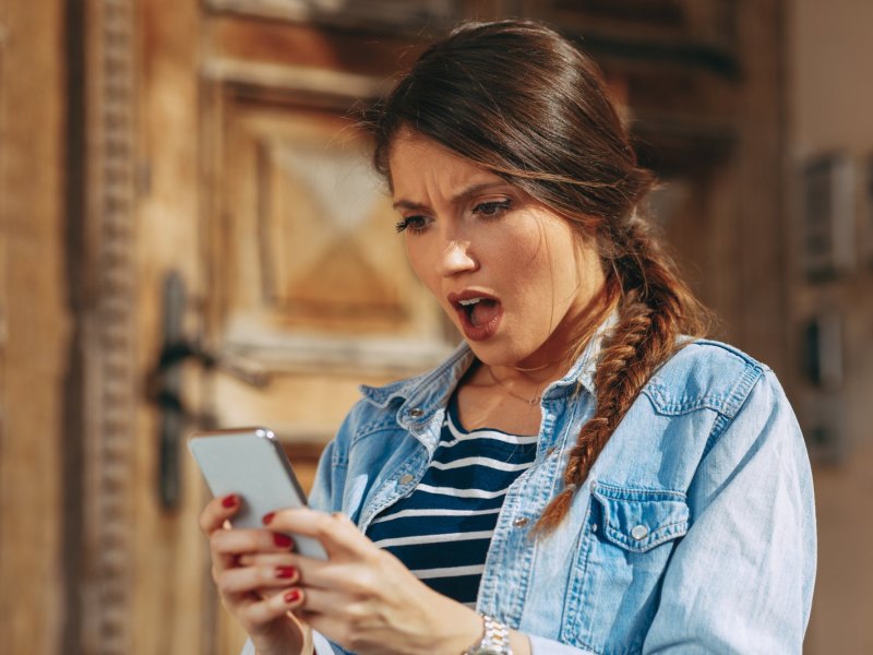 Frau schaut schockiert und wütend auf ihr Handy.