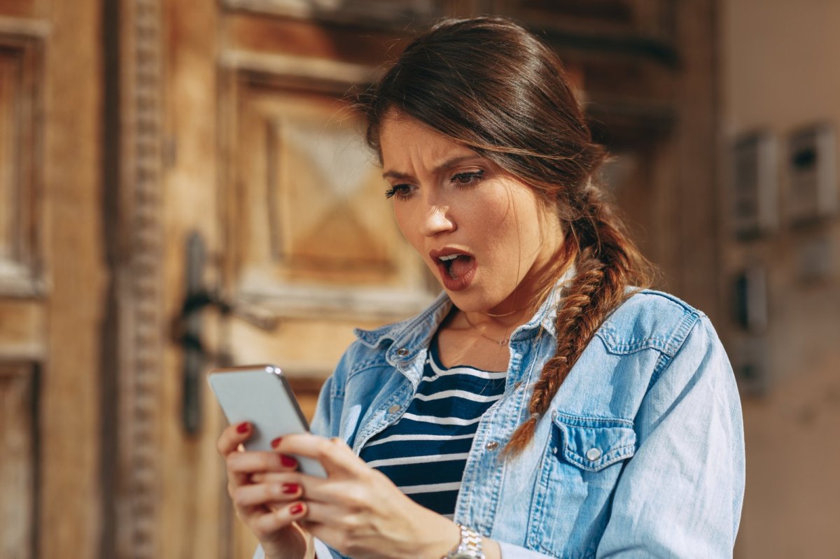 Frau schaut schockiert und wütend auf ihr Handy.