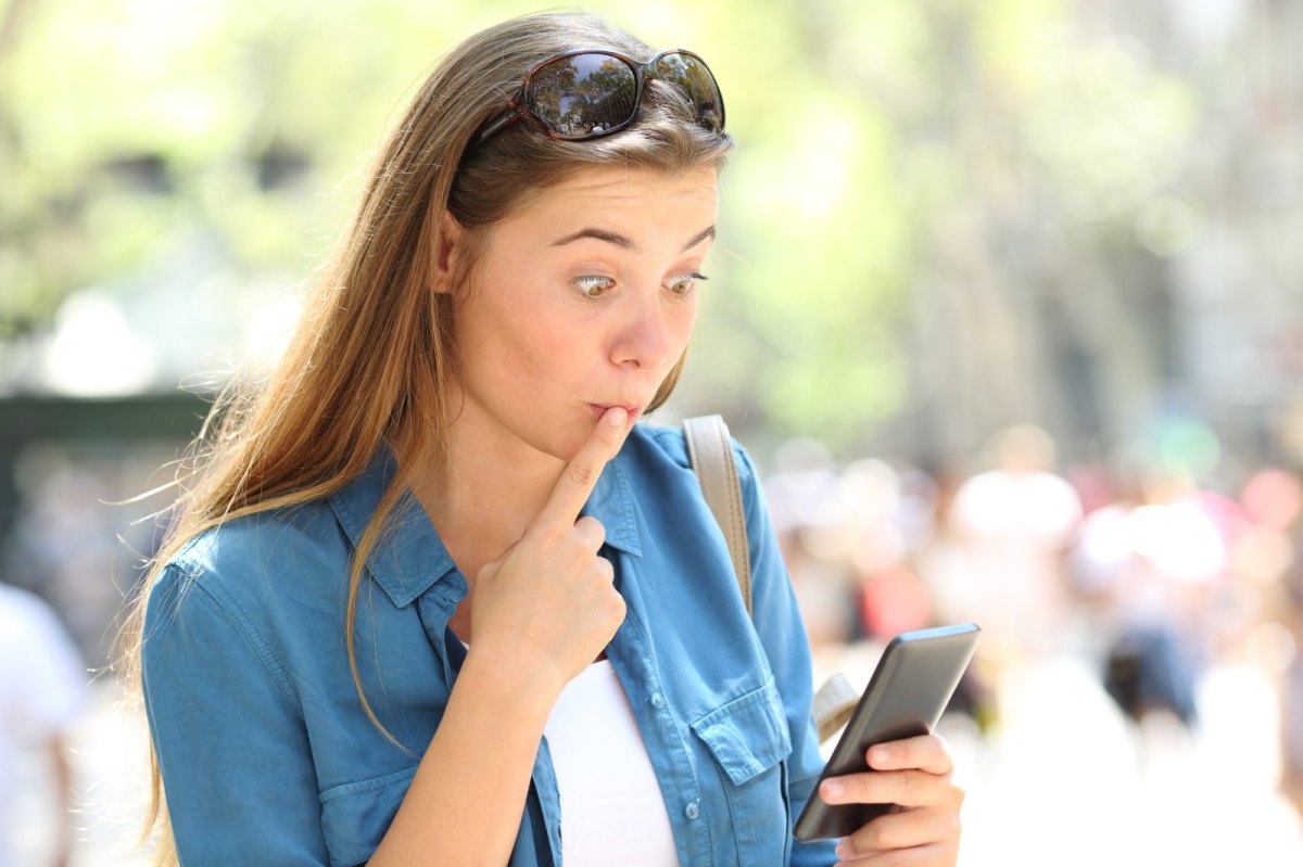 Eine Frau blickt peinlich berührt und schockiert auf ihr Handy.