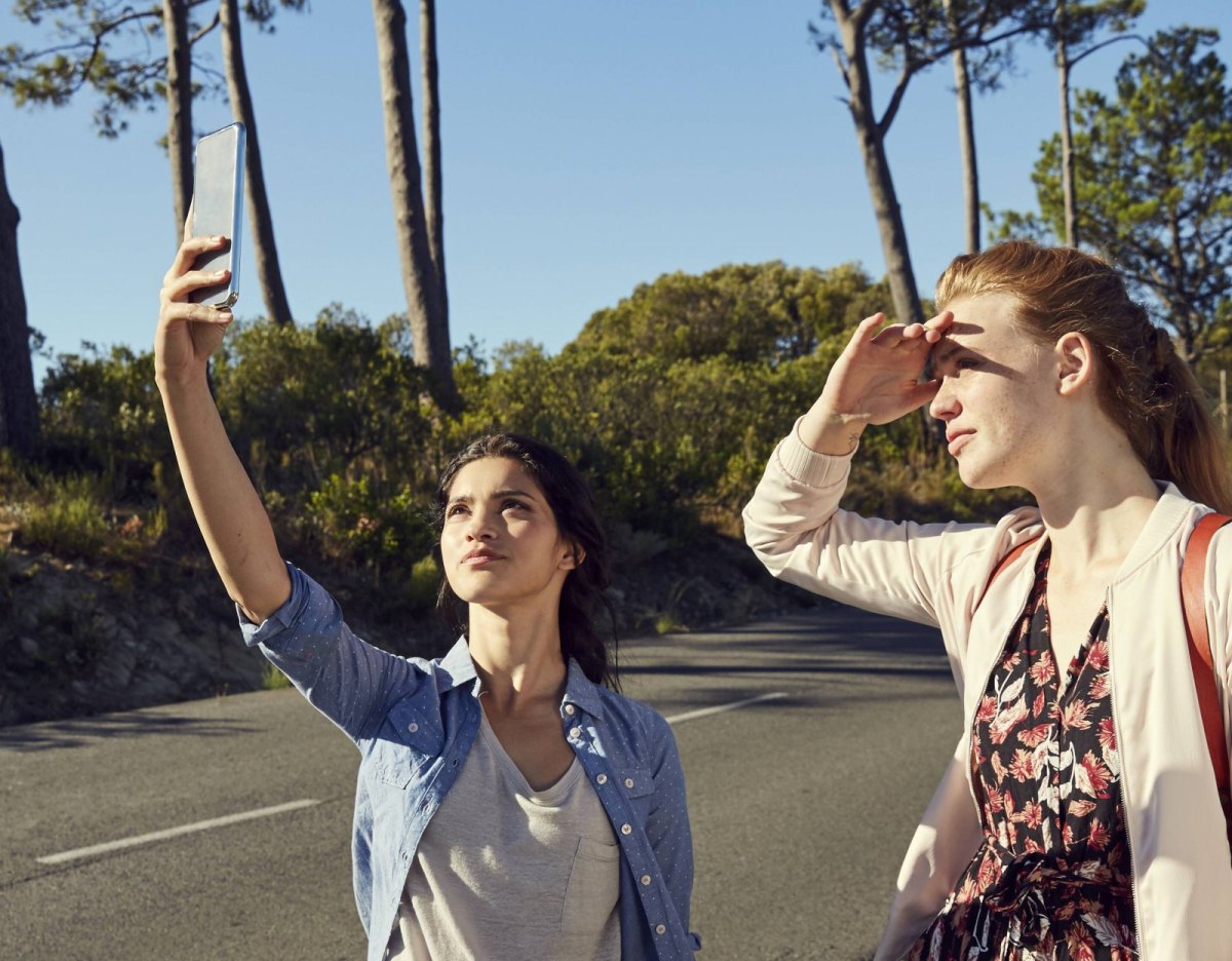 Zwei junge Frauen halten am Straßenrand suchend ihre Handys in die Höhe