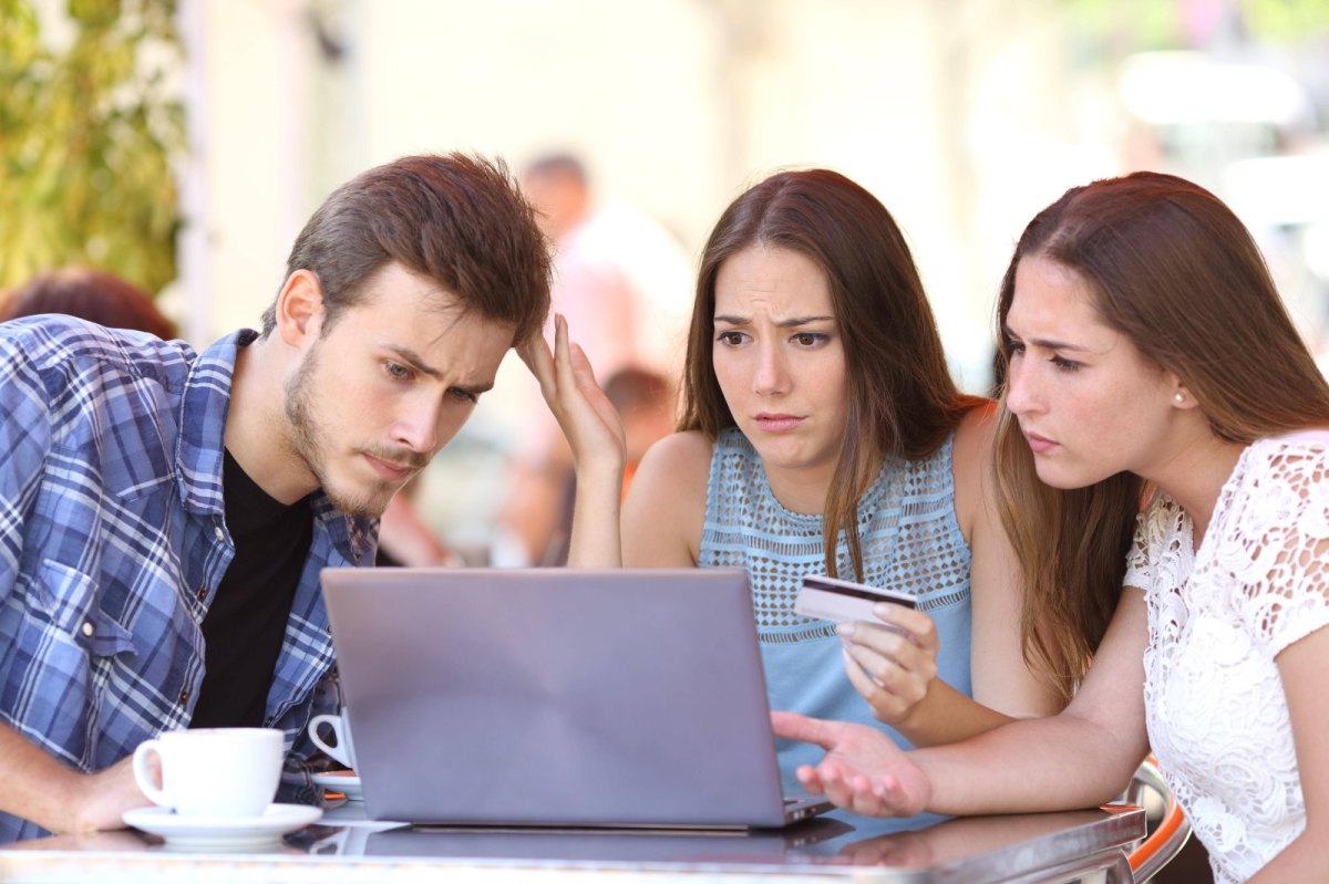 Drei junge Menschen sitzen vor einem Laptop und sind verwundert über ein Online-Shopping-Erlebnis.