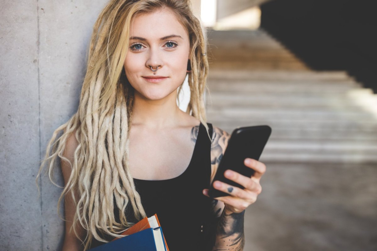 Junge Frau in einem Universitätsgebäude mit Büchern und Handy.