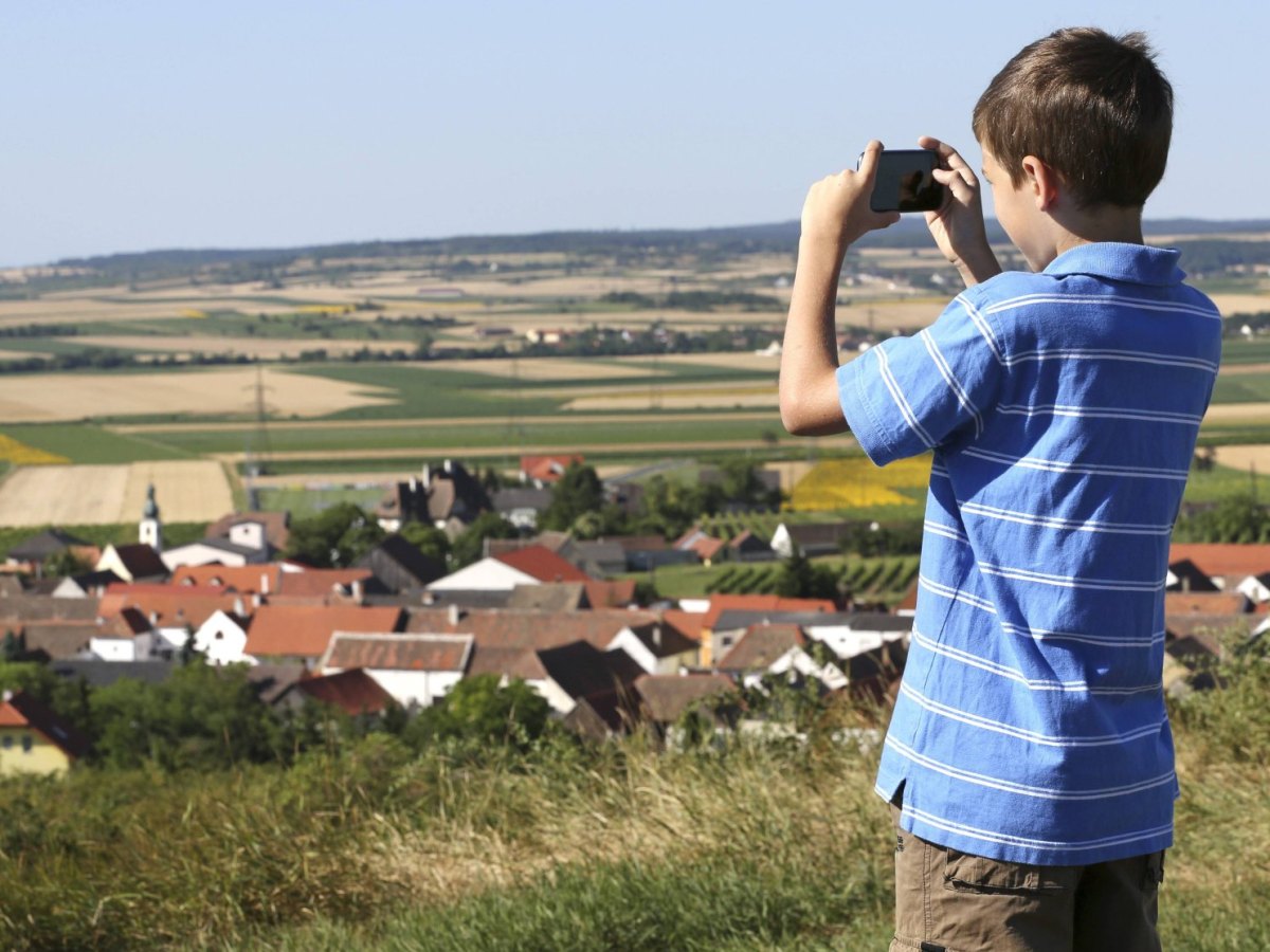 Junge mit Smartphone auf einem Hügel.