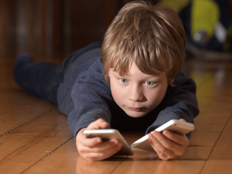 Junge liegt auf dem Boden und hält zwei Smartphones in der Hand