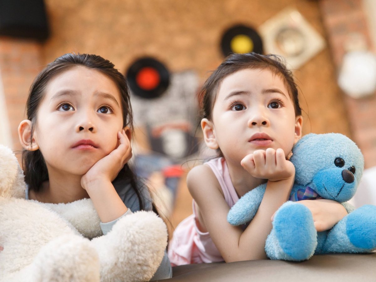 Zwei Kinder liegen auf dem Bett und gucken Fernsehen.