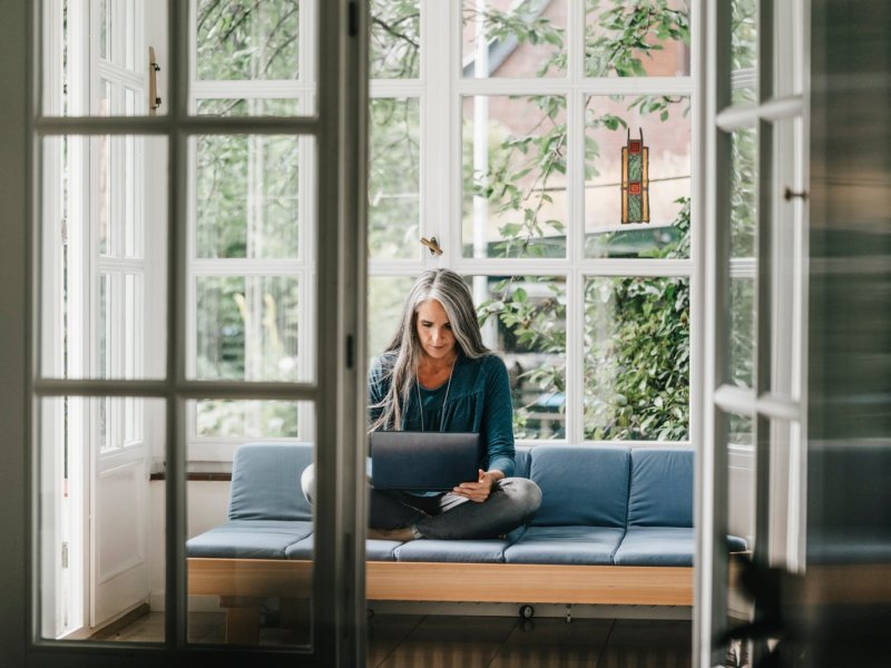 Frau sitzt auf dem Sofa mit Laptop.