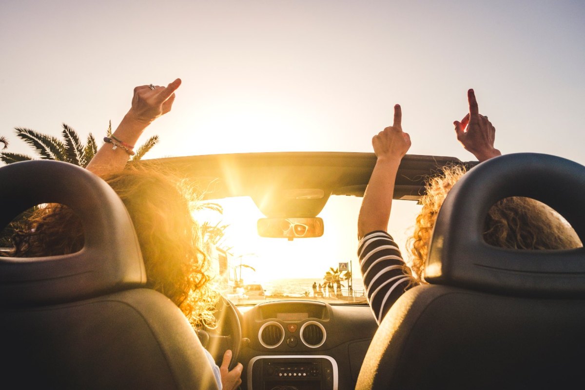 Menschen im Auto von hinten heben fröhlich die Arme in die Luft.