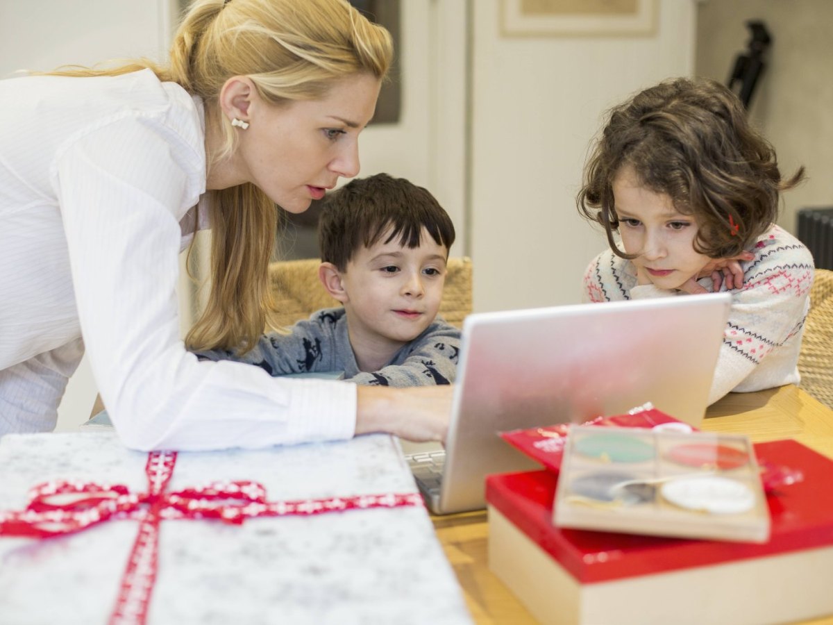 Eine Mutter schaut mit ihren Kinder am Küchentisch auf einen Laptop.