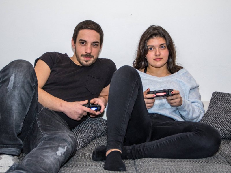 Junger Mann und Teenager Mädchen spielen mit PlayStation 4 Controllern auf Couch daheim Videospiele spielen auf Konsole