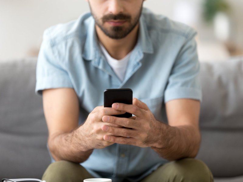 Mann mit Smartphone sitzt auf einem Sofa