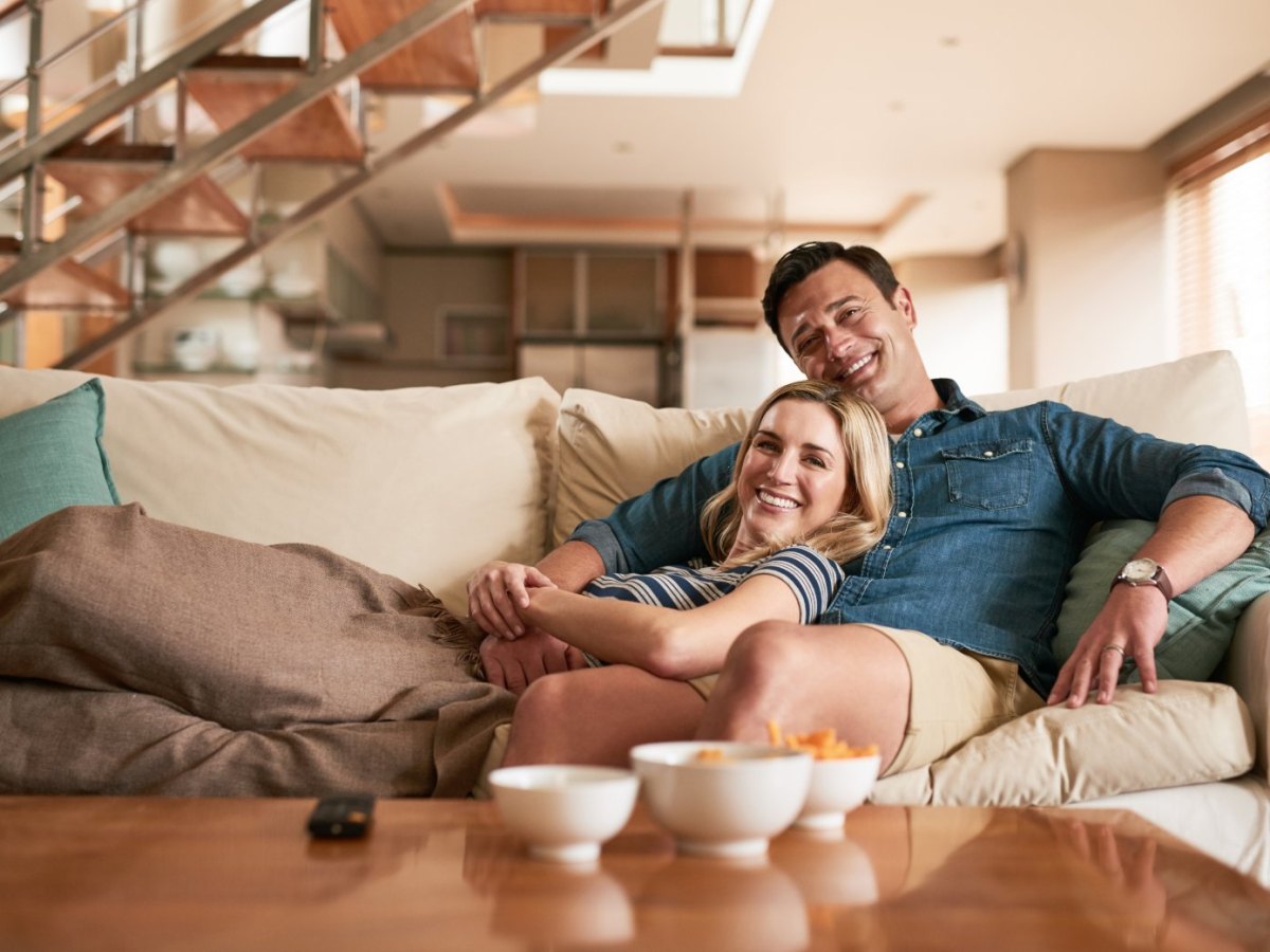 Mann und Frau liegen auf dem Sofa und schauen Fernsehen.