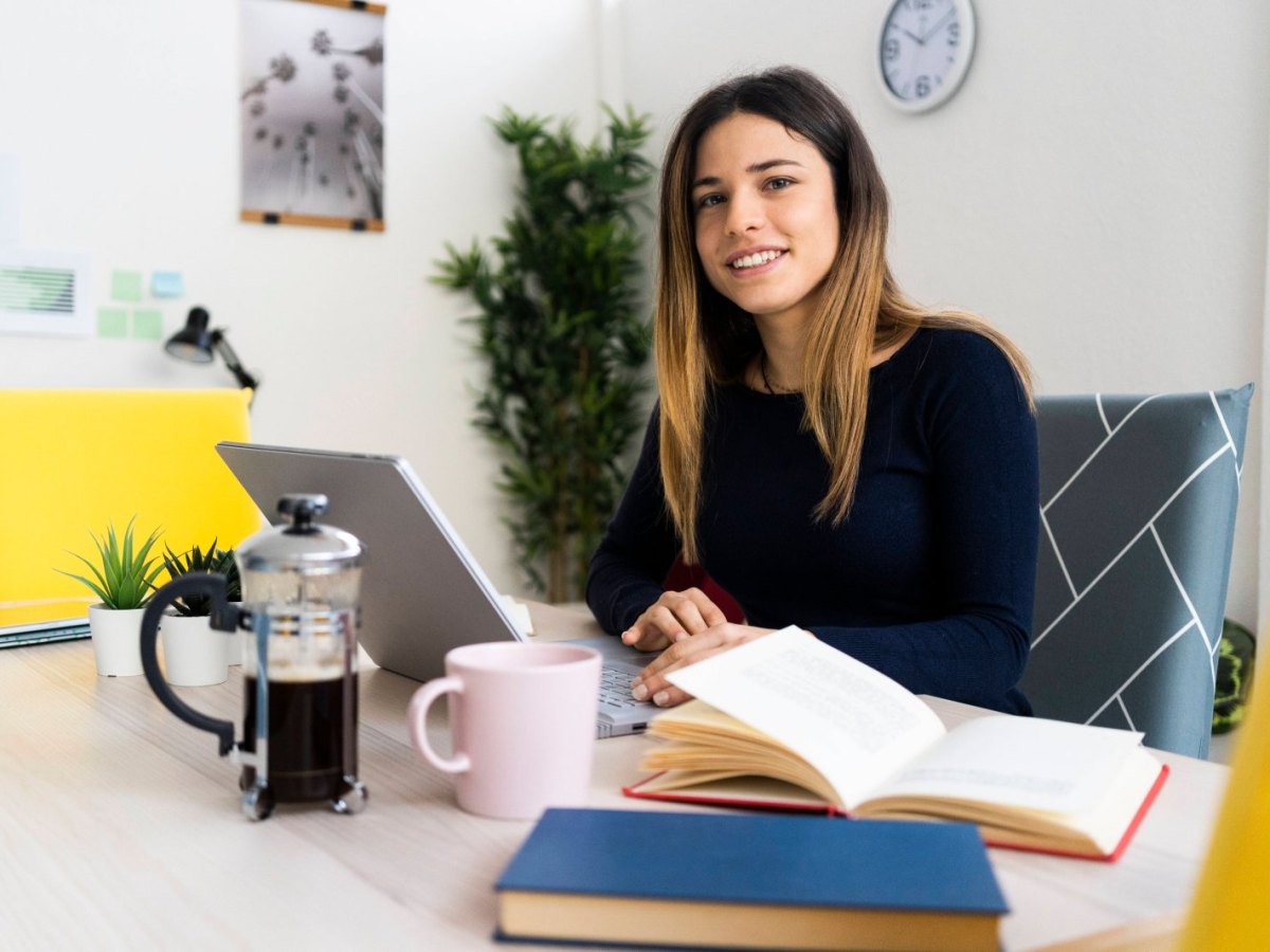 Junge Frau sitzt zu Hause an ihrem Schreibtisch und arbeitet am Laptop.