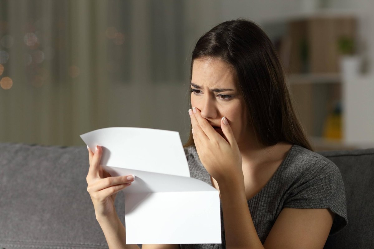 Frau hält ein Blatt Papier in der Hand und schaut geschockt drauf.