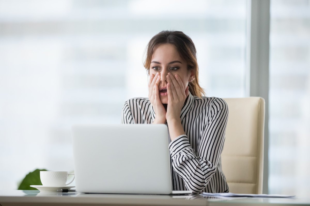 Junge Frau sitzt geschockt vor ihrem Laptop.