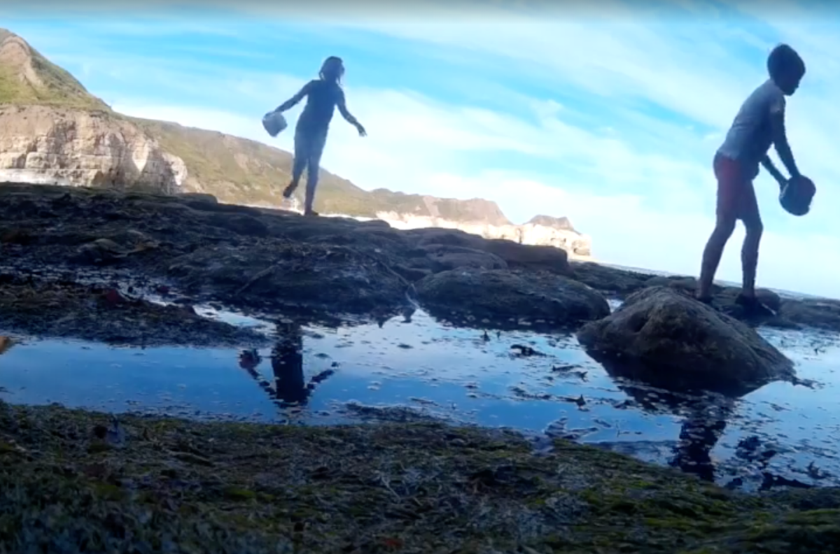 Ein Screenshot aus dem Video zeigt den Jungen und eine Freundin beim Spielen am Strand.