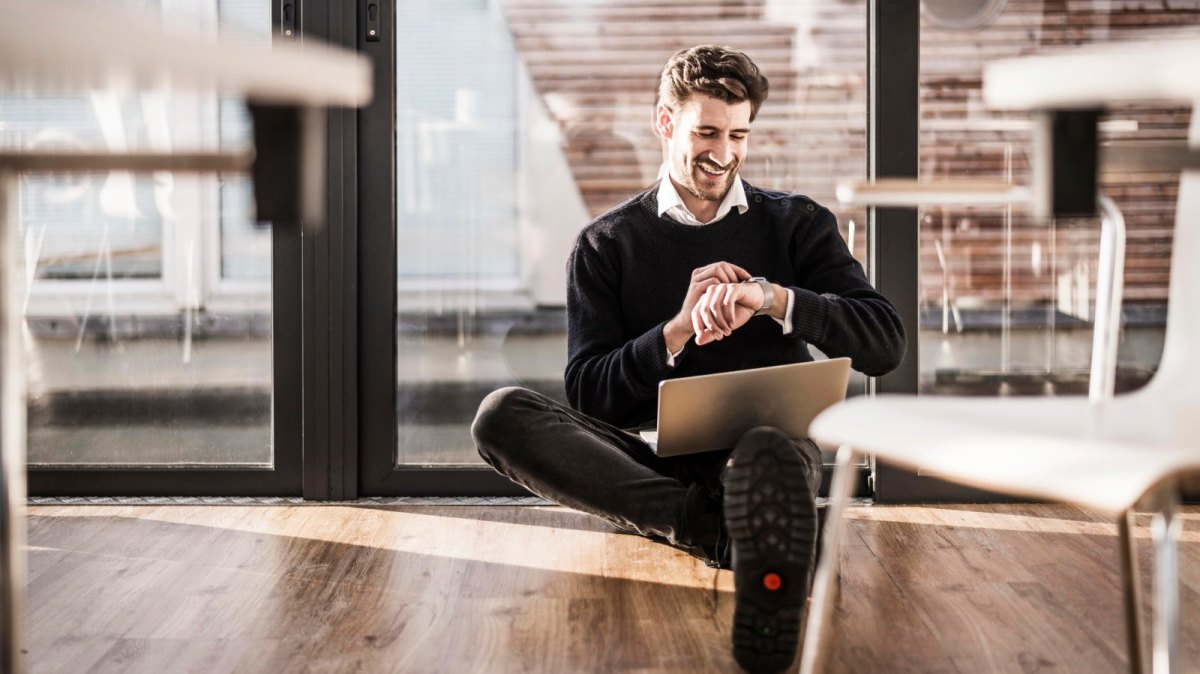 Mann mit Laptop und Smartwatch sitzend.