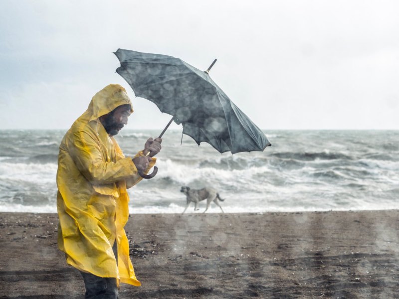 Mann in Regelmantel und Starkregen am Strand.