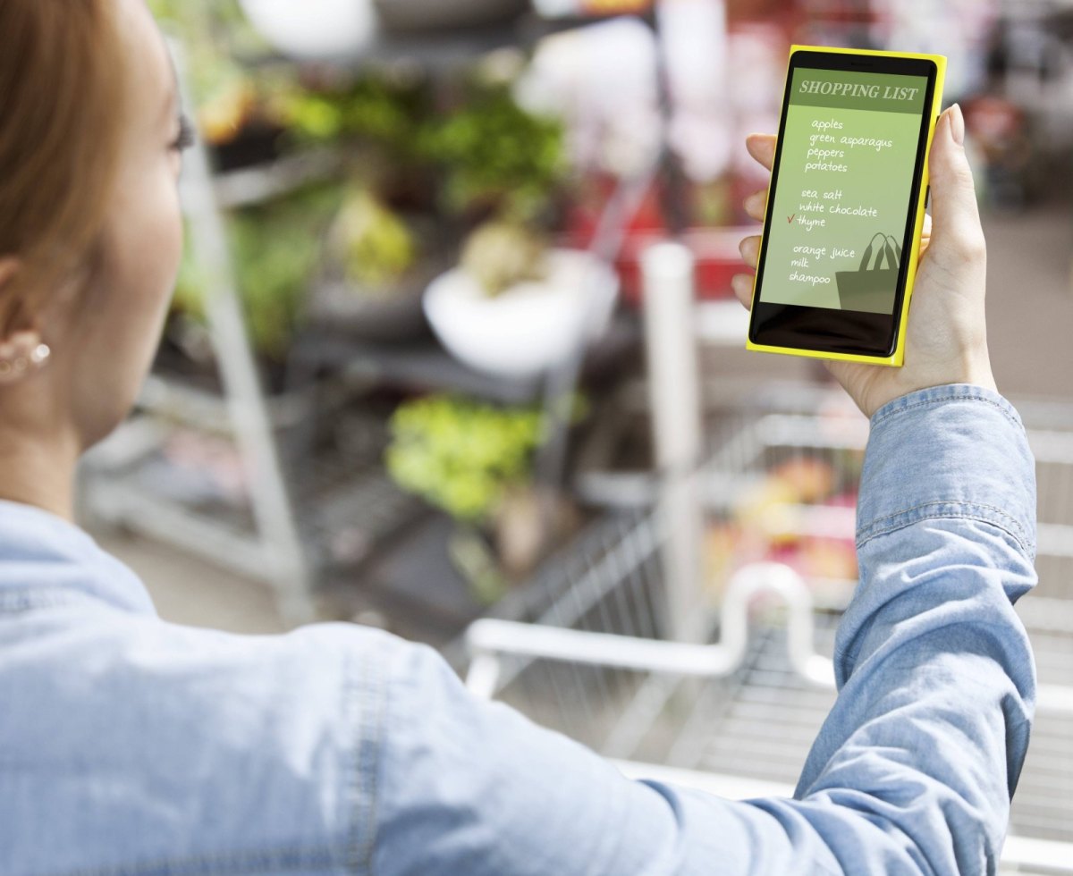 Eine Frau schaut im Supermarkt auf ihr Smartphone.