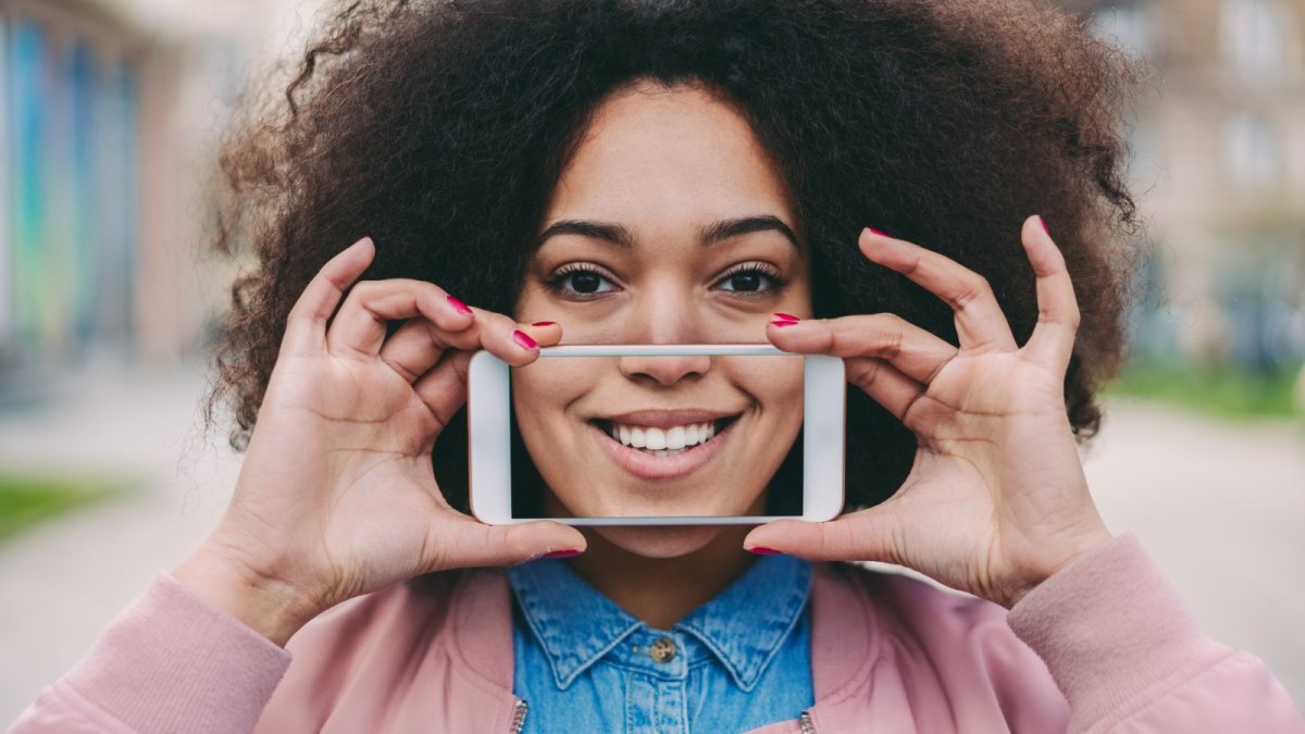 Frau hält Smartphone vor Zähne