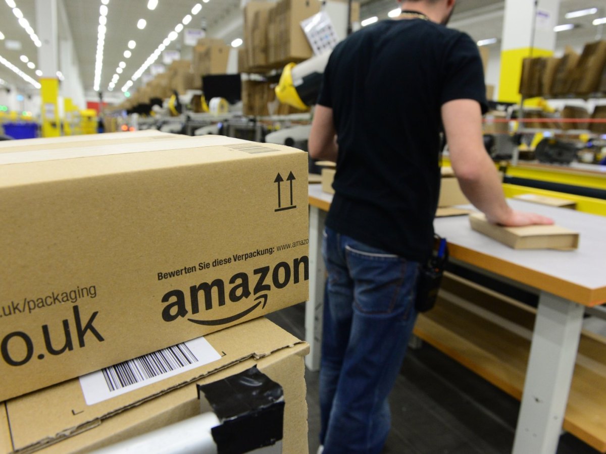 Mann in Logistikzentrum von Amazon mit Amazon-Paket im Vordergrund