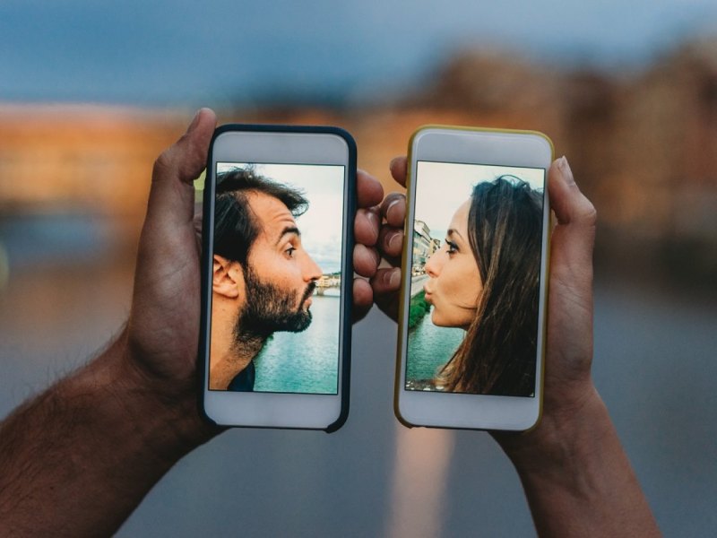 Pärchen küsst sich über ein Handy.