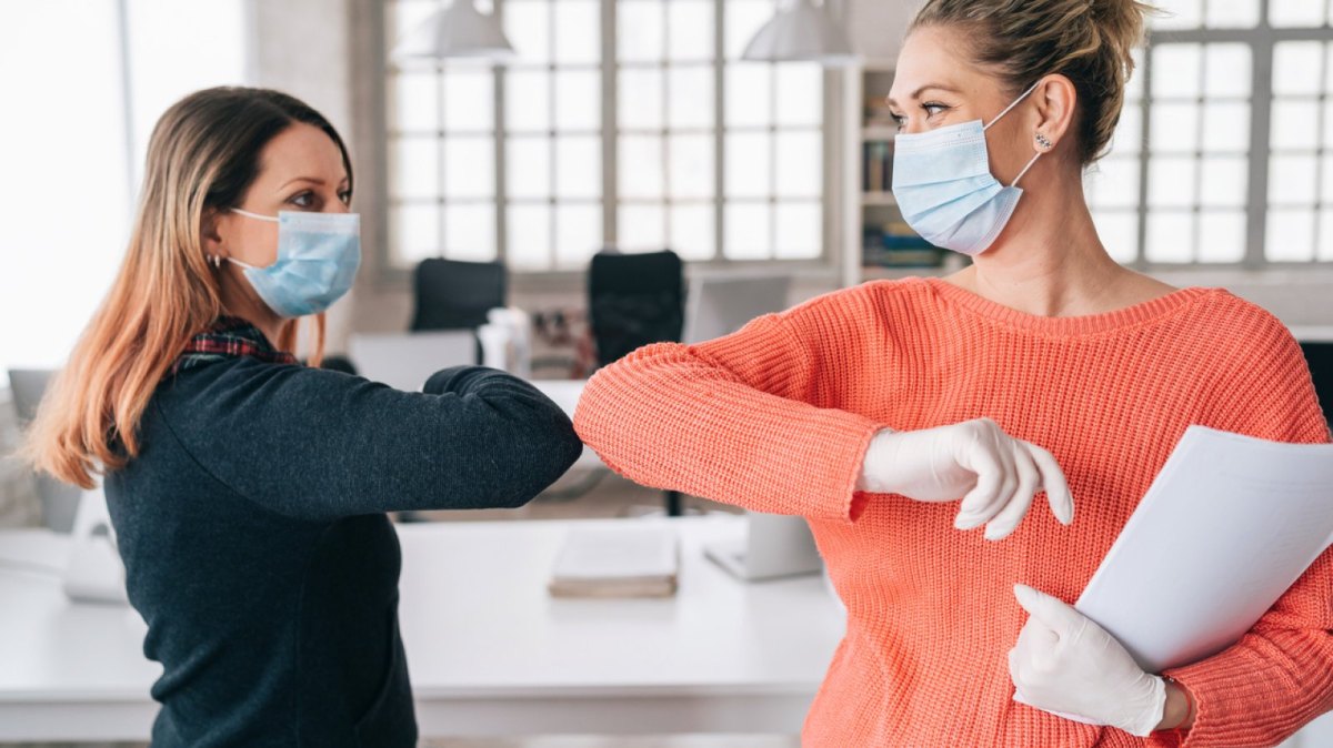 Zwei Frauen mit Mundschutz begrüßen sich mit den Ellenbogen.