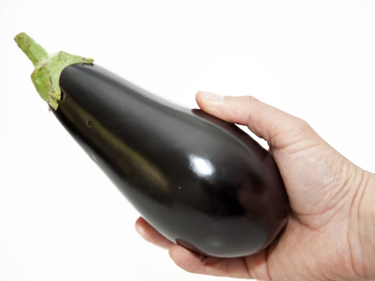 Eine Mann hält eine Aubergine in der Hand.