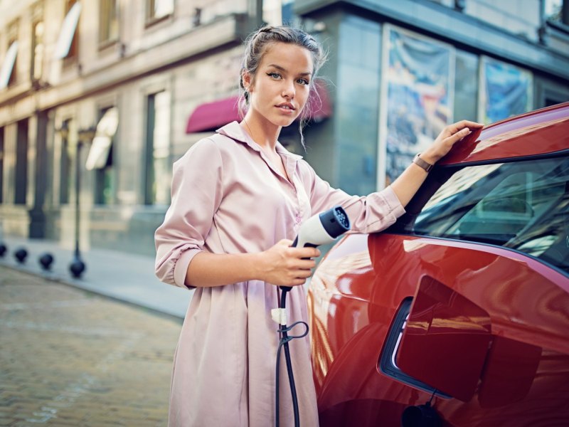 Eine Frau steht mit einem Ladegerät an einer Ladestation für ihr Elektroauto.