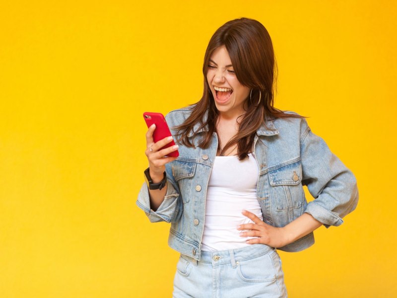 Frau blickt beeindruckt auf ihr Handy und stemmt eine Hand in die Hüfte.