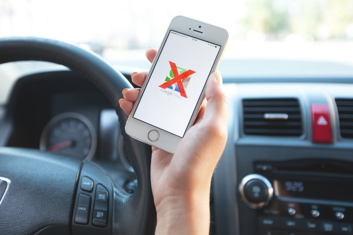 Frau hält Handy mit Google Maps-Logo im Auto in der Hand.