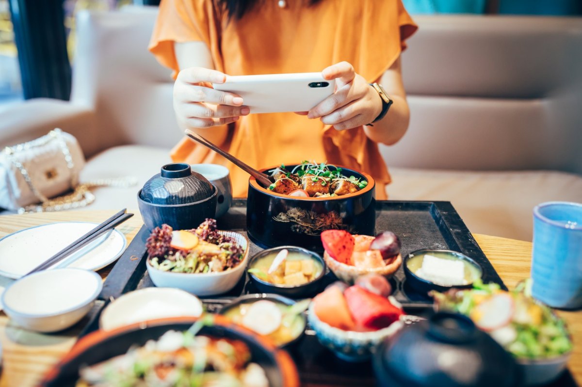 Frau macht ein Foto von asiatischem Essen.