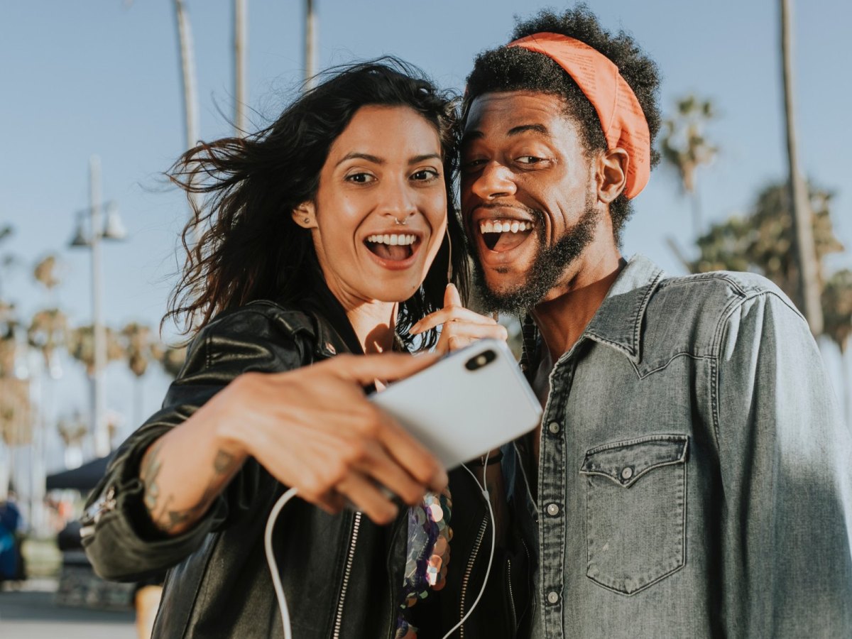 Zwei junge Menschen machen ein Selfie auf einer Strandpromenade.