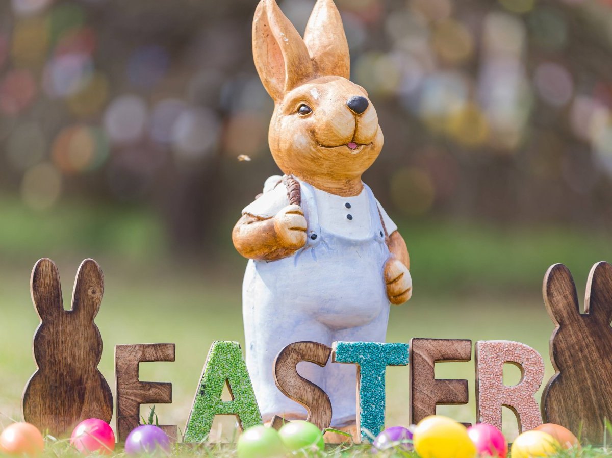 Osterhase steht hinter "EASTER"-Schild und Eiern.