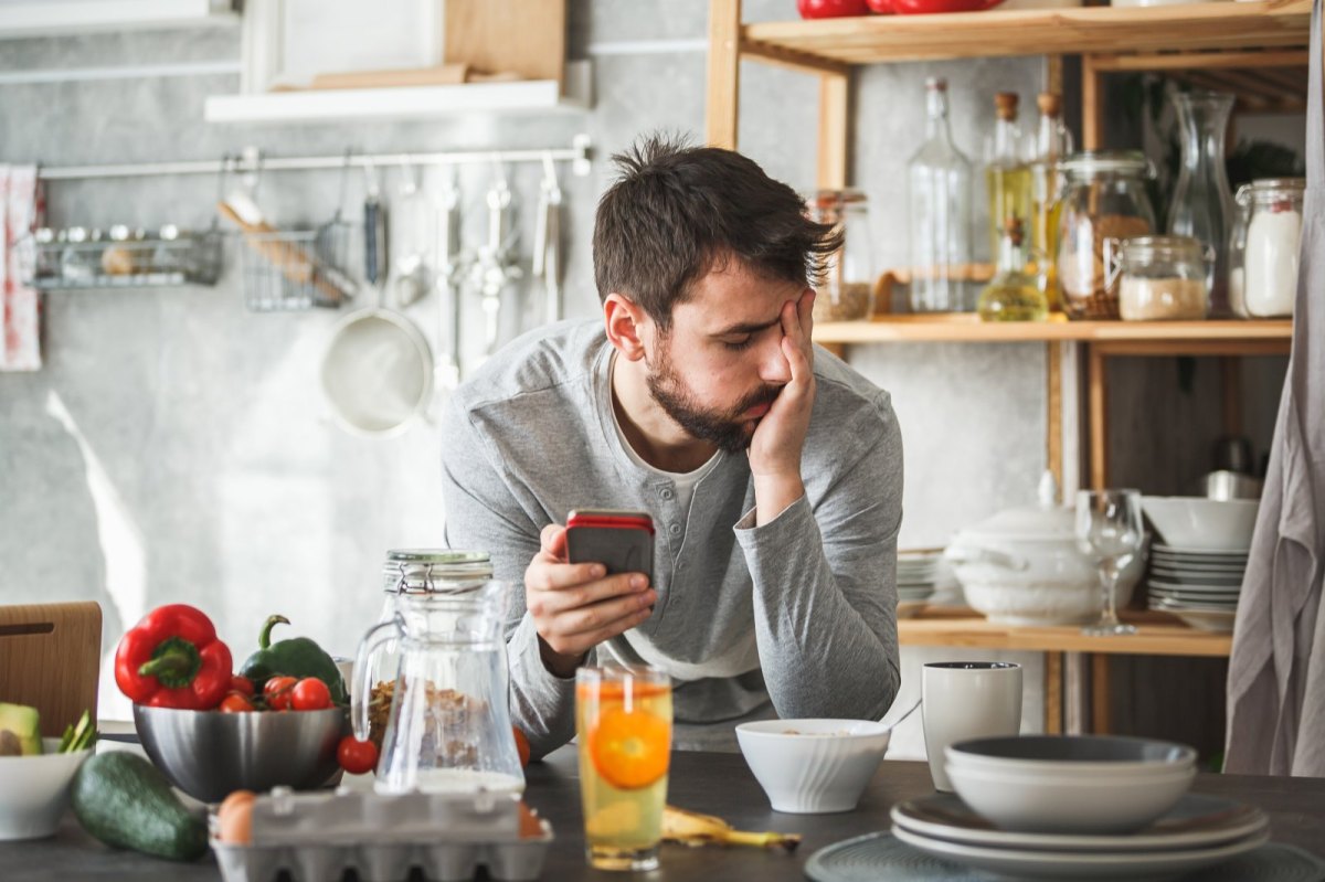 Mann genervt mit Handy in seiner Küche.