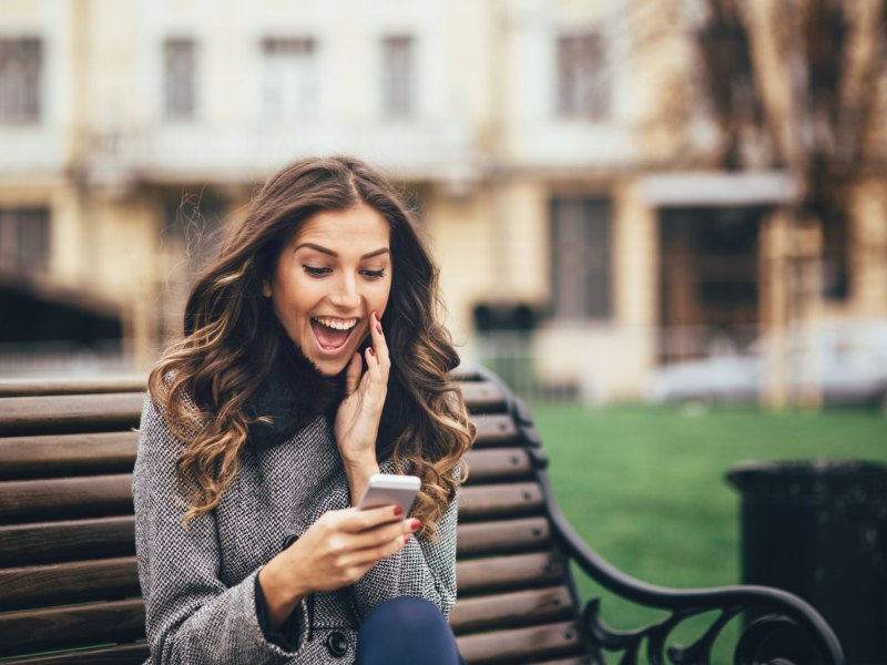 Frau schaut freudig überrascht auf ihr Handy.