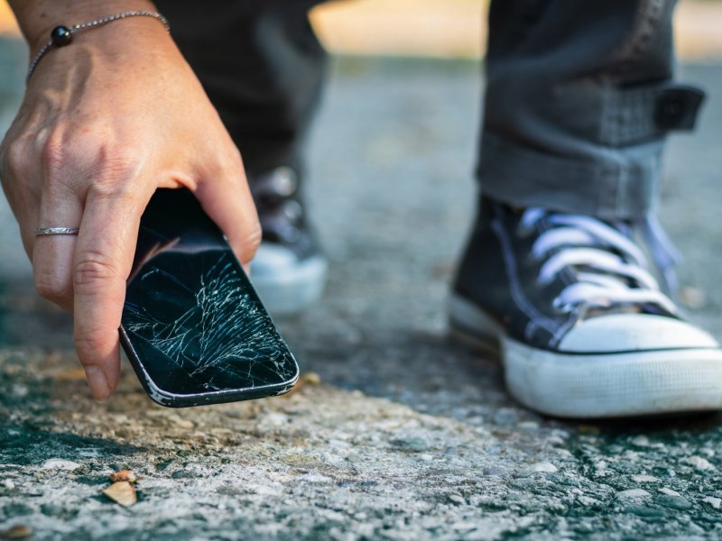 Ein Smartphone mit einem gerissenen Bildschirm liegt auf dem Boden