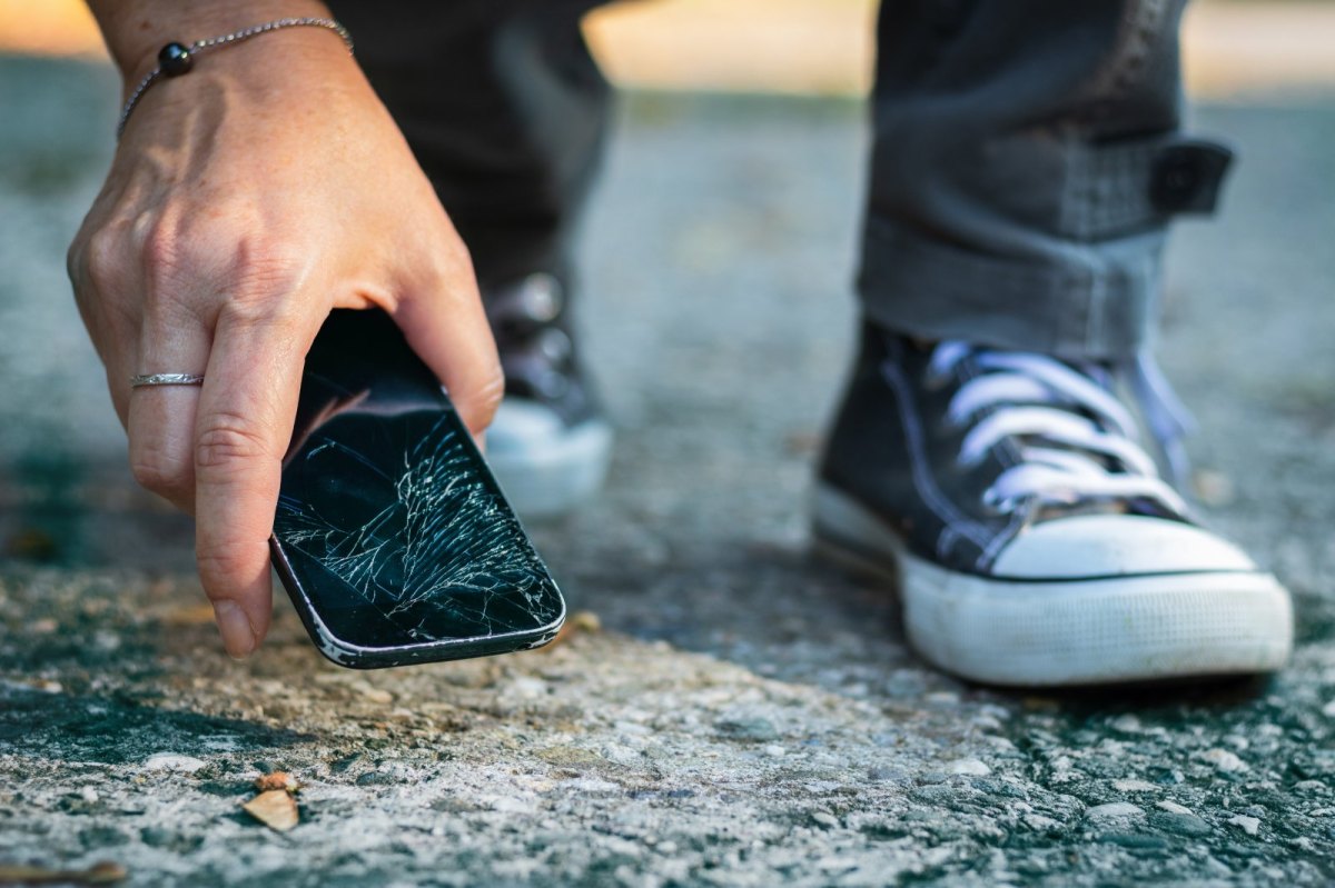 Ein Smartphone mit einem gerissenen Bildschirm liegt auf dem Boden