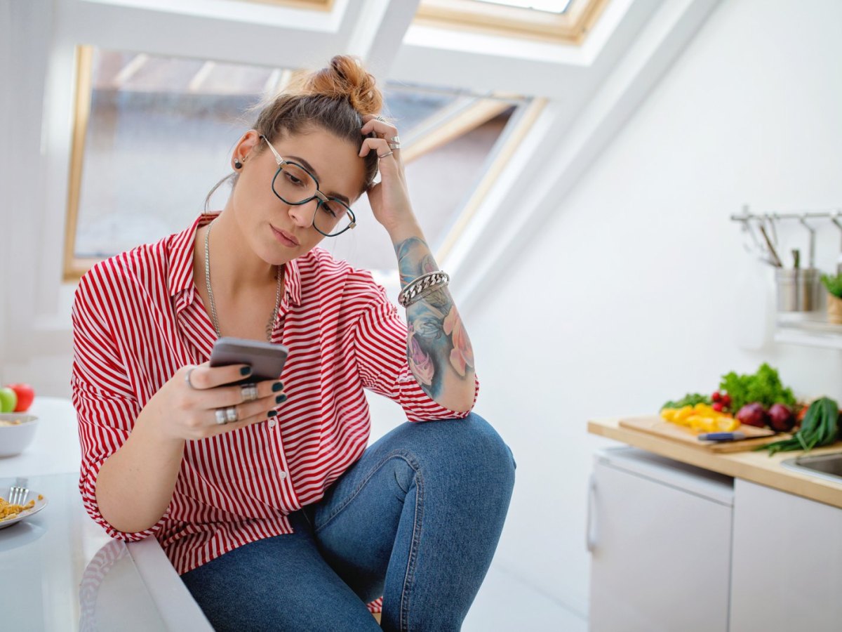 Frau schaut nachdenklich auf ihr Handy.