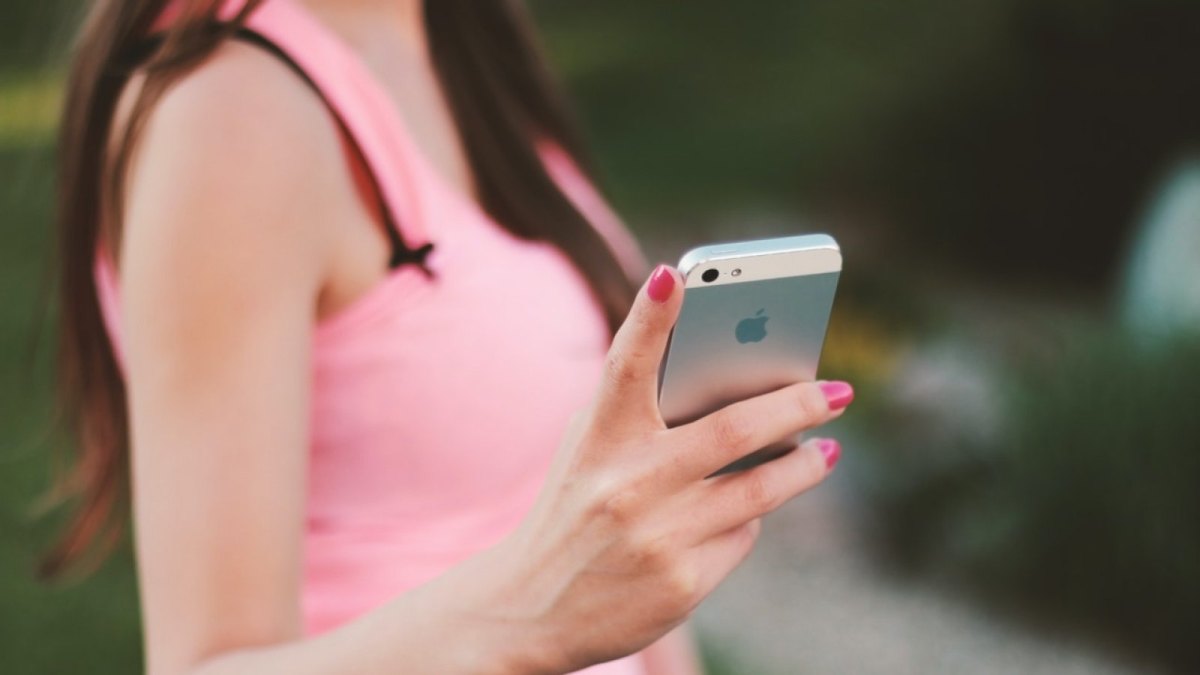 Eine Frau in einem rosafarbenen Shirt hat ein IPhone in der Hand.