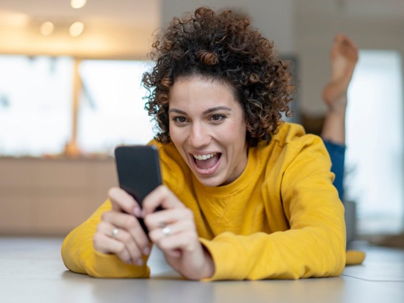 Frau schaut begeistert auf ihr Handy.