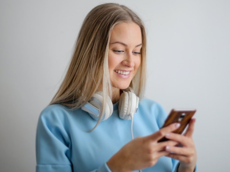 Eine Frau lächelt und schaut auf ihr Smartphone.